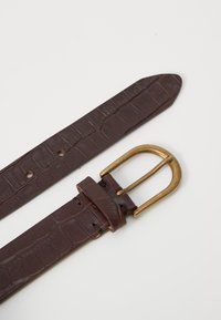 Ceinture en cuir marron avec un motif texturé ressemblant à celui d'un crocodile et une boucle en métal doré. Elle possède une extrémité effilée et plusieurs trous de réglage.