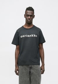 Μαύρο βαμβακερό μπλουζάκι με λευκή επιγραφή "marimekko" στο στήθος, με στρογγυλή λαιμόκοψη και κοντά μανίκια· με λεία υφή.