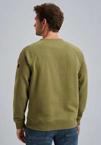 Sweatshirt vert olive avec un col rond, des poignets et un ourlet côtelés. Dispose d'une poche à patch sur la manche gauche. Texture douce.
