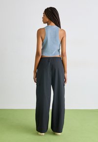Hellblaues, ärmelloses Crop-Top, kombiniert mit schwarzen, lässigen Cargo-Hosen mit weitem Bein und seitlichen Taschen. Glatter Stoff mit lockerer Passform.
