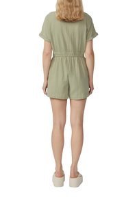 Jumpsuit verde chiaro con maniche corte arrotolate, vita elastica e pantaloni corti morbidi. Tessuto dalla consistenza morbida, indossato con scarpe con plateau.