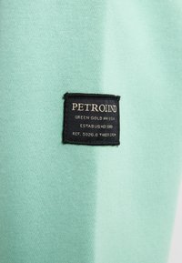 Tessuto verde menta con una finitura testurizzata, caratterizzato da un'etichetta nera con la scritta “PETROLIND” e dettagli in testo dorato.