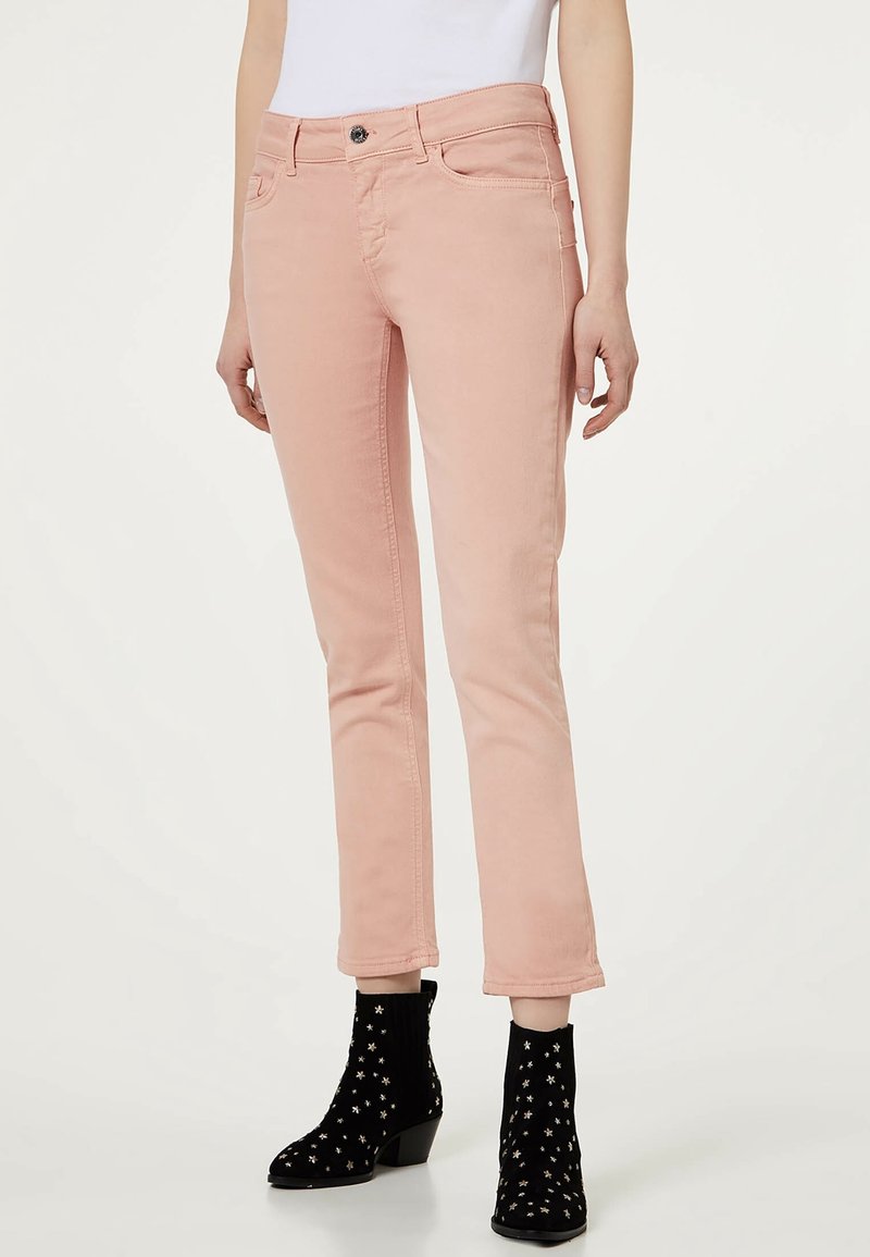 Jean en denim rose à coupe slim, design à cinq poches, avec des détails de couture latérale, associé à des bottines noires à motifs d'étoiles.
