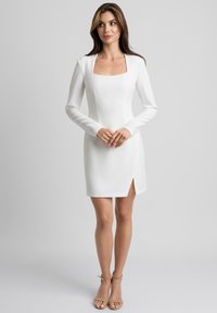 Biała dopasowana sukienka z długimi rękawami, kwadratowym dekoltem i rozcięciem z boku. Gładki, strukturalny materiał. Noszona z beżowymi sandałkami na obcasie.