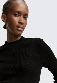 Schwarzer, gerippter Pullover mit langen Ärmeln, hohem Kragen und diagonalen Texturdetails. Der Stoff wirkt weich mit einem leichten Glanz.