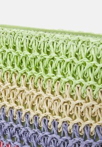 Sac tissé avec des couches texturées en nuances de vert, beige et violet ; fabriqué à partir de fibres naturelles avec un motif de points lâche et ouvert.