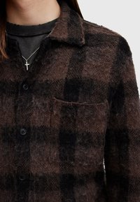 Brun och svart rutigt skjortjacka i mjukt, texturerat tyg med knappar, krage och en enda bröstficka.