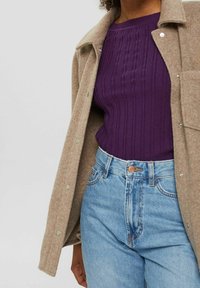 Beige, ullblandad jacka med tryckknappar över en rippad lila topp, parat med ljusblå, högmidjade jeans med knappstängning.