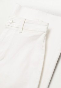 Jean en denim blanc plié, montrant la ceinture avec passants de ceinture et fermeture par bouton en métal sur un fond clair.