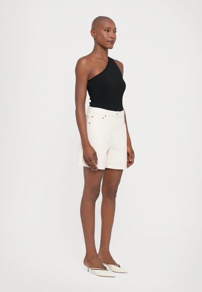 Svart ribbet topp med én skulder, høyt liv hvite shorts og kremfarvede mules med spiss tå. Enkelt design, ingen synlige mønstre eller dekorasjoner.