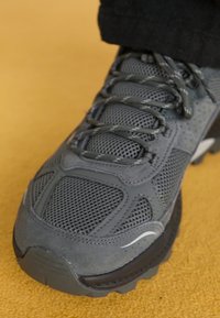 Gray athletic shoe with mesh and suede materials, featuring textured patterns, round laces, reinforced toe cap, and thick rubber outsole.