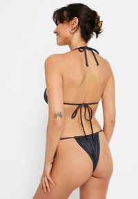 Čierny bikiny set s dizajnom na krku s viazacími popruhmi a riaseným zadným dielom. Hladká látka s minimálnym zakrytím na zadnej strane.