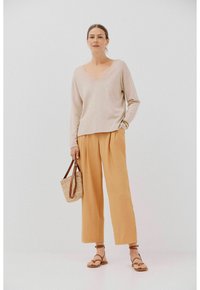 Beige V-hals trui, brede oranje broek en bruine sandalen. Geweven handtas met leren straps. Glad materiaal en relaxte pasvorm.