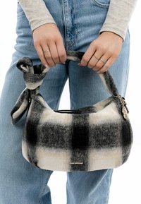 Schwarz-weiße karierte Handtasche mit einer weichen, flauschigen Textur und einem geknoteten Riemen. Verfügt über einen Metallanhänger und einen Reißverschluss.