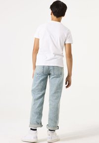 Camiseta blanca de manga corta, jeans azul claro con los puños enrollados y zapatillas blancas con detalles grises, vistas desde atrás.