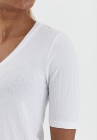Hvid ribbet t-shirt med V-hals og korte ærmer. Stofstrukturen er blød og let, hvilket giver en tætsiddende silhuet.