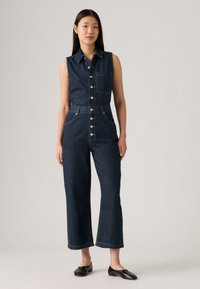 Denim jumpsuit i mørkeblå, uten ermer, med knappelukking foran, brystlomme, vid benkutt, med lys søm og sidelommer.