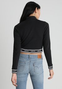 Svart kortärmad topp med lång ärm som har Levi's logotyp längs kanten och manschetterna, tillsammans med ljusblå högmidjade jeans med bakfickor.