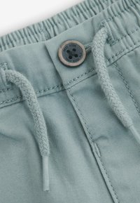 Ljusblå shorts har ett elastiskt midjeband med dragsnören, en svart knapp och en jämn tygtextur.