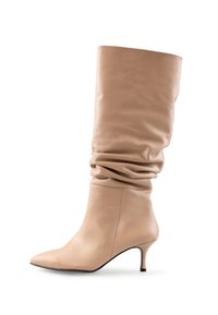 Botine din piele bej, cu un shaft moale, vârf ascuțit și toc subțire de înălțime medie, pe un fundal alb.