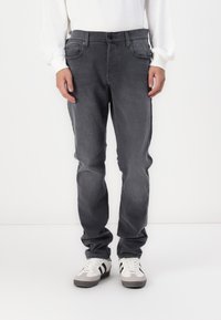 Szürke farmernadrág, slim fit szabással, öt zsebbel, enyhe kopással és standard gombos záródással, fehér sportcipővel párosítva.
