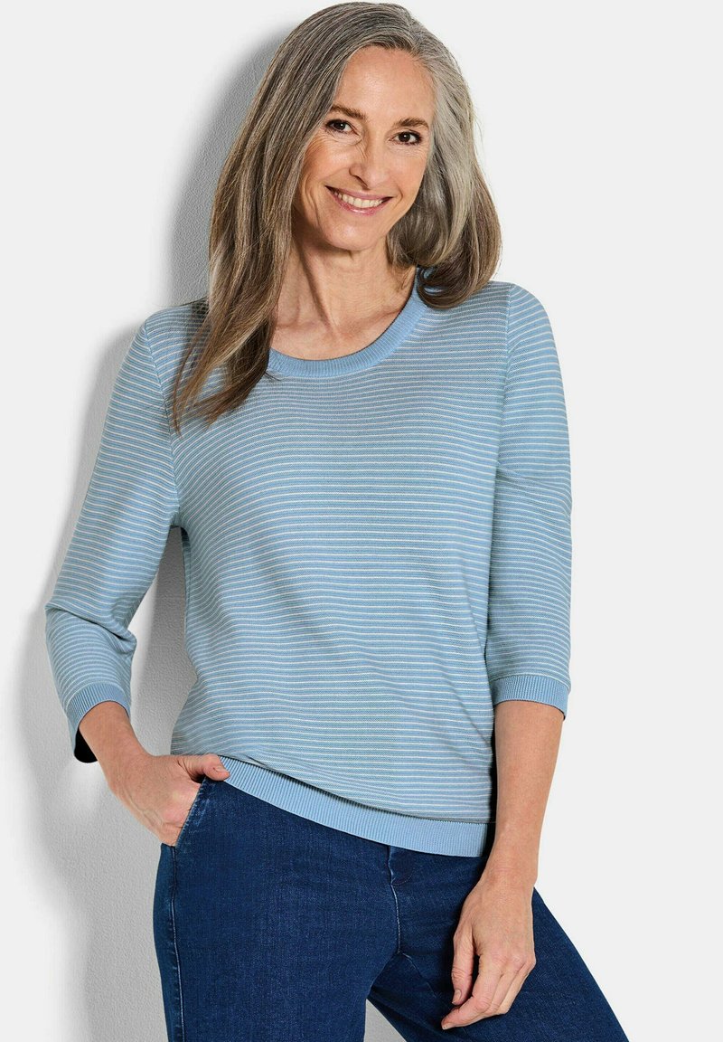 Lichtblauwe gestreepte gebreide trui met een ronde halslijn en driekwart mouwen, gecombineerd met donkerblauwe jeans. Zachte textuur.