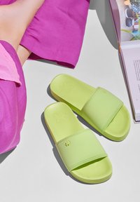 Bright green rubber slide sandals with a double strap, featuring a flower icon embossed on the upper. Set against a light grey background.