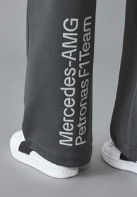 Szare spodnie z napisem "Mercedes-AMG Petronas F1 Team" wydrukowanym białym tekstem po boku, w zestawie z białymi i czarnymi tenisówkami.