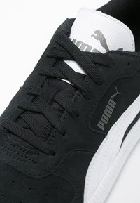 Schwarze Wildledersneaker mit weißer Gummisohle, ausgestattet mit schwarzen Schnürsenkeln, geprägtem Puma-Logo und einer strukturierten weißen Zunge.