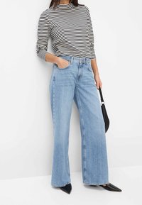 Light blue wide-leg jeans with a high waist and front pockets, paired with a black and white striped long-sleeve top. Black pointed shoes.