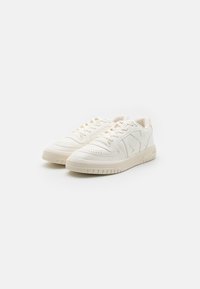 Weiße Leder-Sneaker mit strukturiertem Obermaterial, Perforierungen an der Spitze, flachen Schnürsenkeln und einer dicken Gummisohle mit Rillen.