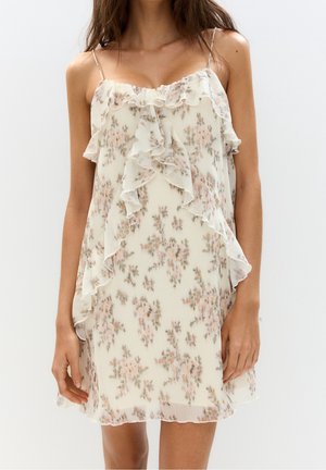 Robe fleurie en tissu léger avec des volants le long de l'encolure et de l'ourlet. Fond pâle avec des motifs floraux roses et verts. Bretelles spaghetti.
