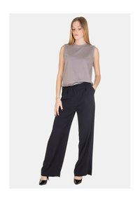 Top grigio senza maniche abbinato a pantaloni larghi neri, caratterizzati da una finitura in tessuto liscio e una vita sagomata. Indossati con décolleté nere.