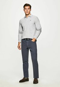 Lys grå langærmet polo-shirt med krave, parret med mørkeblå bukser og brune ruskinds loafers. Minimalistisk design uden mønstre.