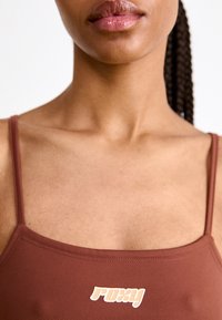 Ruda braletė su plonomis petnešėlėmis pasižymi tekstūruota, elastinga medžiaga ir balta "Roxy" logotipu centre.