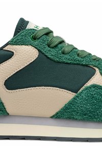 Zapatilla verde y beige con paneles de ante y cuero texturizado, cordones redondos y suela acolchada. Detalles decorativos en la parte superior.