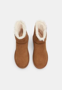 Botoșei de gleznă din suede maro, cu o căptușeală moale din blană sintetică bej și un tiv. Vârf rotund și talpă plată, cu detalii de cusătură.