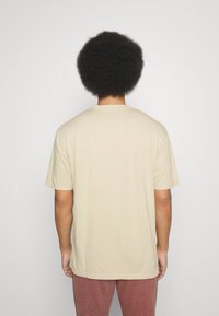 Camiseta de algodón beige con mangas cortas, cuello redondo y un corte relajado. Sin patrones ni gráficos visibles. Diseño simple y tejido ligero.