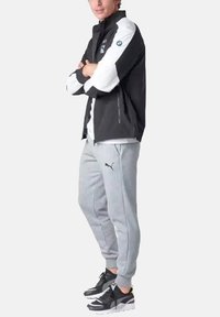 Chaqueta negra y gris con acentos blancos, pantalones de chándal grises y zapatillas negras con suelas blancas. Presenta el logotipo de BMW en la chaqueta.