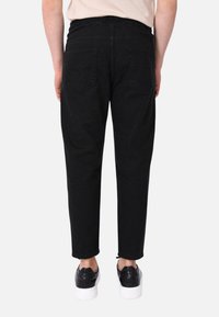 Pantaloni jogger in denim nero con una vestibilità rilassata, cintura elastica e tasche posteriori, abbinati a sneakers nere e una maglietta di colore chiaro.