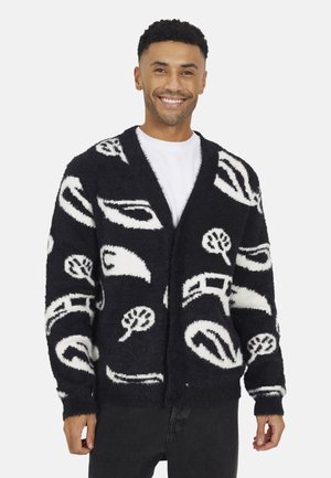 Zwart-witte fuzzy cardigan met abstracte patronen van bomen en vormen, met een sjawl kraag, lange mouwen en knopen aan de voorkant.