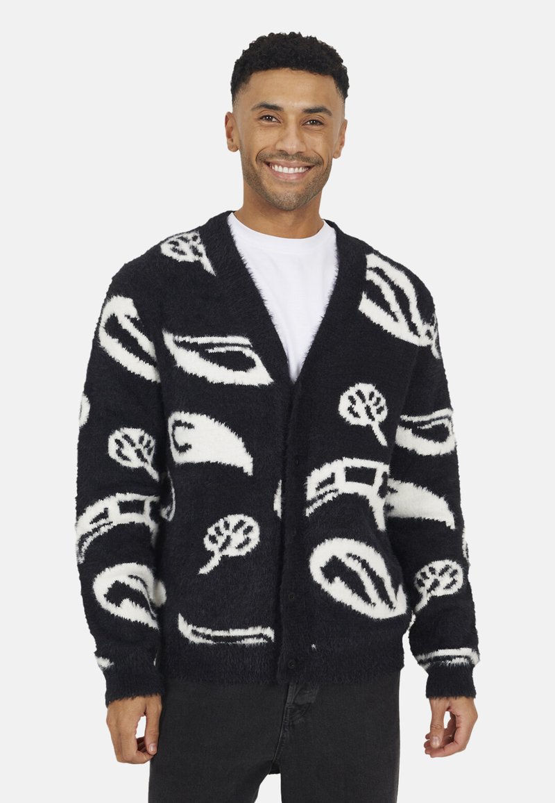 Zwart-witte fuzzy cardigan met abstracte patronen van bomen en vormen, met een sjawl kraag, lange mouwen en knopen aan de voorkant.