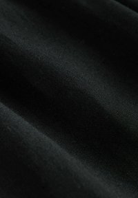 Černá textilie s hladkým, mírně texturovaným povrchem, s jemnými variacemi a záhyby v látce.