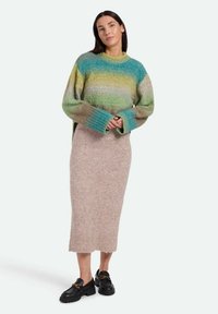 Pulover tricotat cu un gradient de verde și albastru, croială lejeră, manșete largi, asociat cu o fustă tricotată bej și pantofi slip-on negri cu accente aurii.