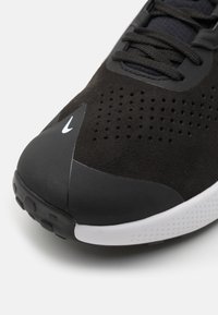 Schwarzer Sportschuh mit Obermaterial aus Wildleder und Mesh, perforiertem Design, gepolsterter Sohle und weißen Akzenten an der Zwischensohle und dem Logo.