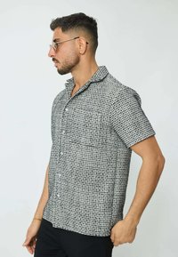 Chemise à manches courtes avec un motif tissé noir et blanc, col, poche avant et boutons. Fabriquée dans un tissu léger, coupe décontractée.
