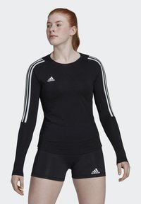 Schwarzes langärmeliges Sportoberteil mit weißem Drei-Streifen-Design an den Schultern und kleinem Adidas-Logo auf der Brust, kombiniert mit schwarzen Shorts.
