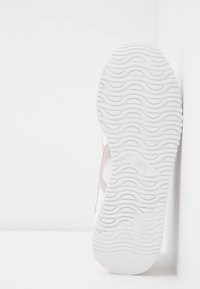 Semelle de basket blanche avec motif ondulé, chaussure légèrement inclinée sur un fond blanc uni.
