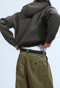 Oversized dark gray hoodie with a drawstring hood, worn over a white t-shirt, paired with olive green trousers featuring back pockets.