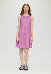 Ärmelloses, knielanges Kleid in einheitlichem Pink mit geraffter Taille und Bindeband am Ausschnitt. Kombiniert mit blauen Sandalen mit Schnallenakzenten.